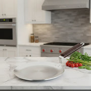 Stainless steel tawa with wooden handle on marble countertop in modern kitchen with fresh vegetables